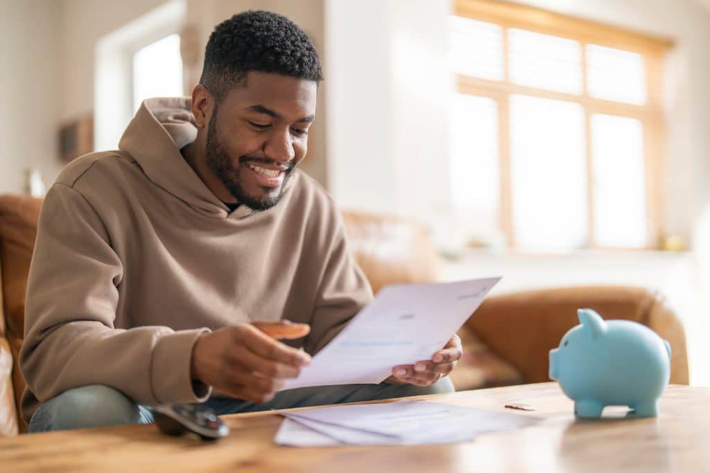 A man smiles as he reviews his finances, papers in hand, with a piggy bank nearby. Gibsland Bank community involvement